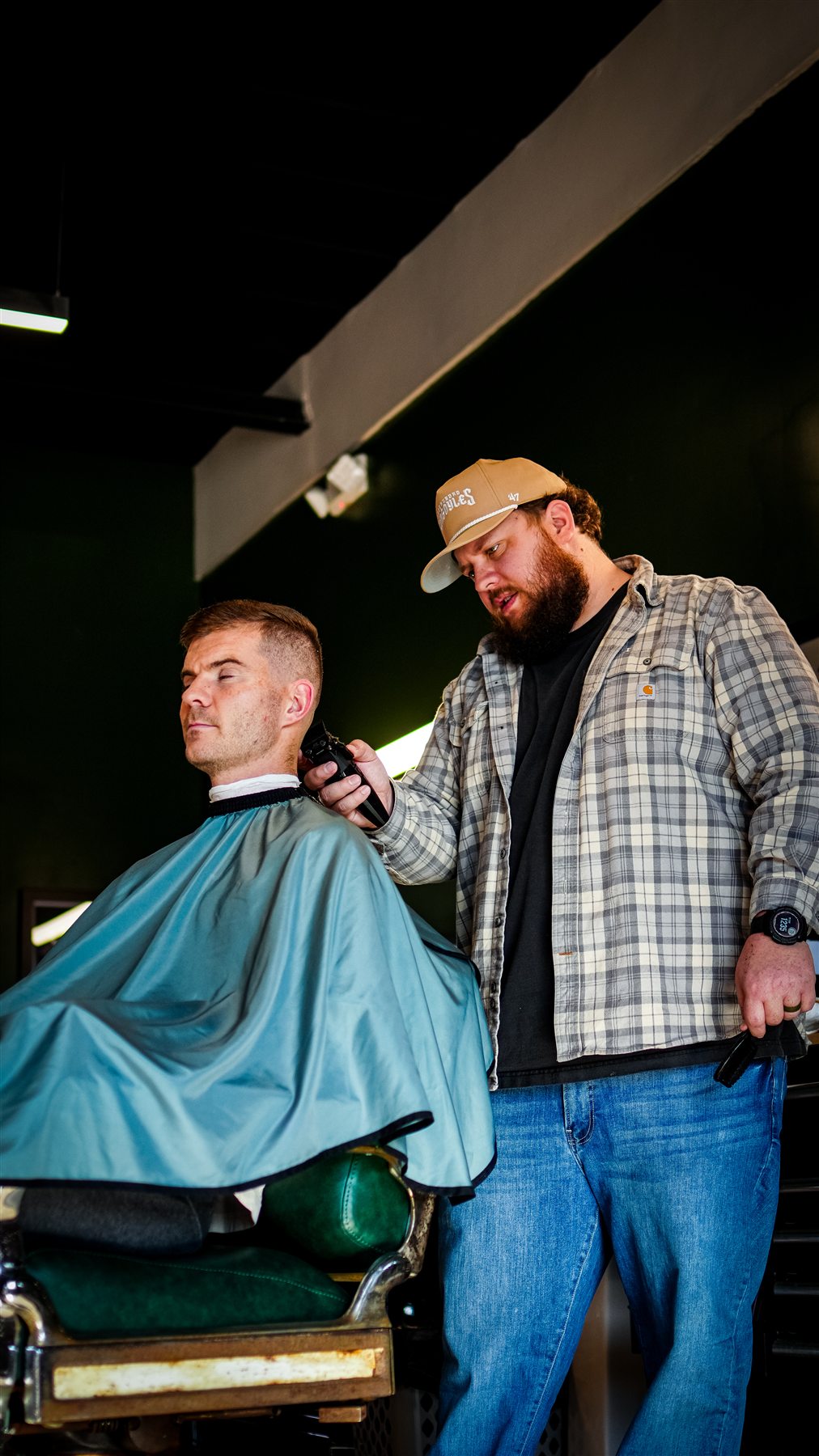 A barber working with a client inside the green-walled shop